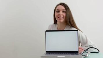 Young Caucasian woman doctor sitting at desk in cabinet and chatting on laptop computer. Female medic blogger showing pills to webcam and blogging on health online. Medicine advertisement. video