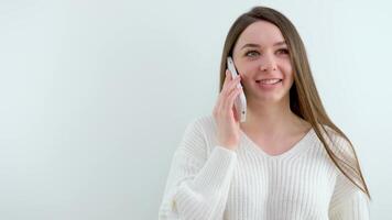 een aantrekkelijk jong vrouw is pratend Aan de telefoon staand geïsoleerd over- grijs achtergrond video