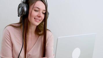 cámara despacio hace zoom en en cara alegre caucásico mujer en auriculares teniendo en línea llamada en computadora portátil, sentado en silla milenario dama participativo en seminario web, comunicado remotamente en Internet video