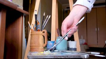 Young craftswoman in apron paints clay vase with paintbrush after baking and handmade shaping in studio. Woman enjoys painting earthenware vase in workroom for handmade pottery shop closeup video