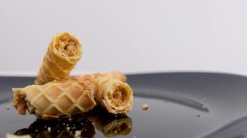 waffle rolls delicious crispy shortcrust pastry in baking tubes with condensed milk boiled condensed milk inside the dessert female hands break up crumbs and fragrant sweetness on a black plate video