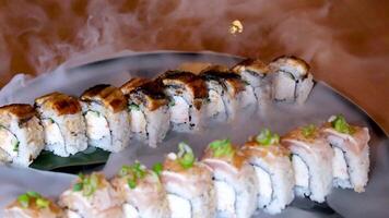 Composition of different kinds of sushi rolls placed on black stone board. Chopsticks and soy sauce bowl on side. Top angle view. video