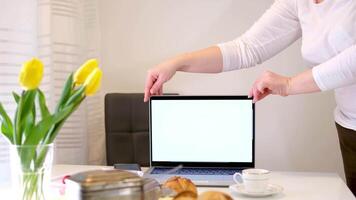 female hands adjusting monitor pointing a finger at ad Yellow tulips laptop with screen for advertising buns a cup of coffee or tea on a white background space for text beauty Tenderness home comfort video