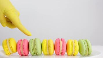 macaroons lögn på de tabell en hand i en gul handske är hölls och sätter ett av dem reklam en Kafé där är en plats för text på en vit bakgrund färgrik franska efterrätt sötsaker video