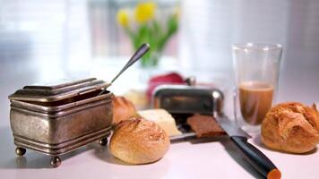 Europese ontbijt licht Toneelstukken langzaam beweging suiker kom onvoltooid koffie in een glas eigengemaakt kaas brood, traditioneel braziliaans tussendoortje Aan de ontbijt tafel in een rustiek boerderij keuken. voorkant visie video