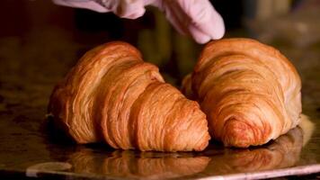 chef com luva mãos tocante dois croissants jogando apertando examinando levantando pratos colocando costas delicioso francês Comida cozimento cozinhando servindo em retroiluminado pedra Castanho prato fechar video