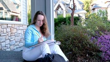 Young woman writing in diary on grass at park. Slow motion footage video