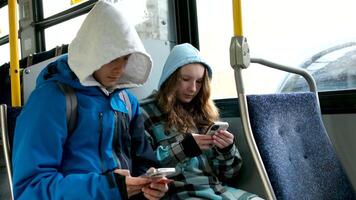 deux adolescents dans bleu vêtements asseoir sur une autobus Canada Vancouver hottes l'automne hiver printemps survêtements utilisation une mobile téléphone chercher pour géolocalisation Voyage les voyageurs réel la vie video