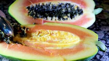 I remove papaya seeds with a spoon on a black background. Dolly slider extreme close-up. video