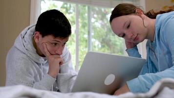 Two caucasian children watching something funny on laptop. Attractive brunette boy pointing his hand on screen. Pretty little girl laughing from what she see on computer video