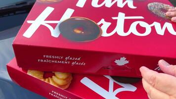 Large, open box of Tim Horton's donuts in contrasted light, with a variety of different donuts. a woman's hand opens and closes a box of sweets lying in the foreground of the car video