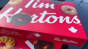 Large, open box of Tim Horton's donuts in contrasted light, with a variety of different donuts.a gift treat on the car is two red boxes with sweets video