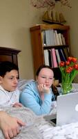 Two caucasian children watching something funny on laptop. Attractive brunette boy pointing his hand on screen. Pretty little girl laughing from what she see on computer video