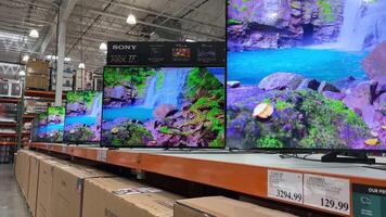 Costco Wholesale sale of televisions stand in row of boxes, as well as demonstration of quality of image on technology monitors in supermarket store selection of visible price tag video