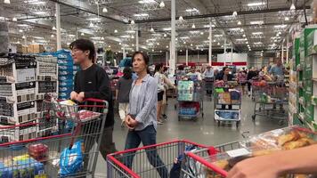 Costco Wholesale shopping in a huge supermarket people walking by with carts choosing goods high ceilings in the store different food on the counter rushing women and men wholesale America Canada video