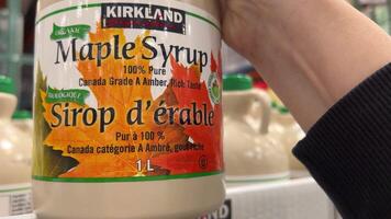 Costco Wholesale buy maple syrup in the supermarket a lot on the shelf in boxes a large selection to take by hand put one bottle in the cart video