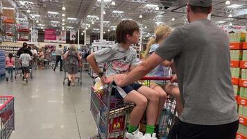 Costco Wholesale father pushes teenagers children on shopping cart buys groceries other people pass by life in supermarket mop floor special machine janitor slow motion of huge store video