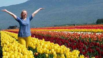 vuxen kvinna i fält av tulpaner kläder blå gul tycka om flagga av ukraina glädje lycka i bergen blomning gul blommor frihet friskhet luft gul byxor blå blus ljushårig vanlig kvinna video