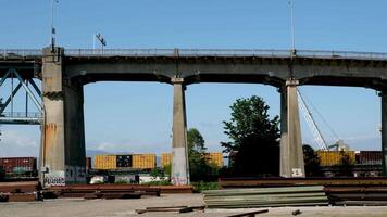 Pattullo Bridge over Fraser River train passing under bridge. close-up shot from technological site scattered iron beams for the construction of new bridge against the backdrop of mountains and sky video