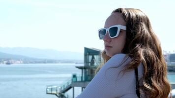 Jeune attrayant souriant fille regards par élégant des lunettes de soleil en mettant sur leur dans ensoleillement fermer en plein air. magnifique rêveur visage profiter se détendre, marrant vacances, bonheur contemplation sur ensoleillé journée video