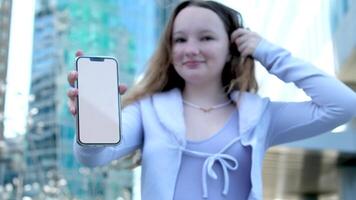 against the backdrop of a skyscraper in downtown Vancouver, a young girl shows a phone with a white screen recommends a trip space for text smile lilac clothing color teenager video