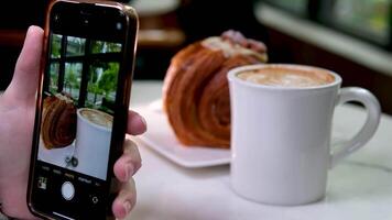 over- de schouder schot van vrouw handen maken foto mobiel inhoud van koffie video