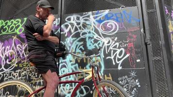 haasten straat Vancouver een Mens Aan een fiets tegen de achtergrond van een geschilderd muur in ivan Kuvere rookt sigaretten drug oud kleren pet shorts zomer straat in dakloos werkloos werkloosheid kont video