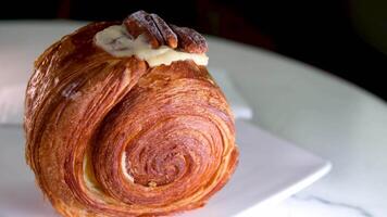 Nahansicht Aussicht von ein frisch und lecker Croissant Lügen auf das Weiß Teller mit Blumen- Ornament und rotierend auf das hölzern runden Tafel. Lager Filmaufnahme. Konzept von Bäckerei und Gebäck video