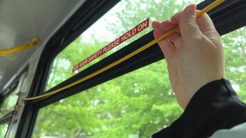 To stop Canadian buses, you need to pull rope, wire will sound stop signal, woman's hand stops bus, press sign, exit, end the journey, green leaves outside the bus window, Vancouver Canada, Surrey. video