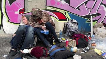 in the alley, a man and woman are lying on asphalt, sleeping, using drugs, dirt, clothes, sneakers, lying around scary picture of unknown sexual orientation against the backdrop of graffiti wall video