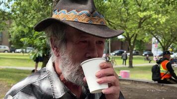 hasting street vancouver elderly man with gray beard drinks tea on the street with a plastic cup paper cup cowboy hat plaid shirt homeless people tea party hot drinks help drug legalization video