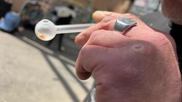 Encendiendo un vaso cigarrillo con drogas ligero un encendedor mano con un anillo de cerca en contra el antecedentes de Vagabundo personas en el callejón masculino sucio vencido mano video