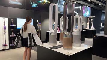 dyson rons. vacuum cleaners and other equipment inside a home appliance store a girl walks around the store looking at the latest technology in the hands of the girl bags of lLuluemon video