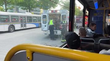 se från de fönster av en buss i vancouver trafik är stannade ambulans plockar upp en person tar bort med blinkande lampor människor se ut de fönster anställda i ljus grön västar paramedics hjälp video