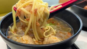 Homemade clear chicken soup with noodles sprinkled with chopped greens in the white bowl on the bamboo table mat, top view close-up video