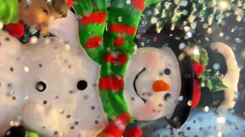 Snow globe with snowman stands between two snow-covered Christmas trees Near him are 3 children who just built him he has a black hat with a green scarf with red stripes Silvery snowflakes fly around video