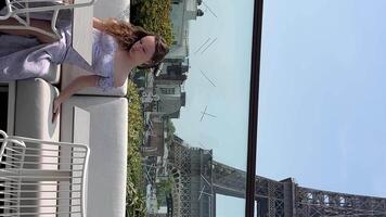 une blond fille dans une longue magnifique robe est assis contre le Contexte de le Eiffel la tour avec une endroit pour texte dans une restaurant surplombant le Eiffel la tour elle penche retour sur le siège video