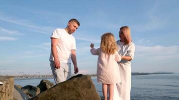 jung glücklich Familie mit das Kind beim Sonnenuntergang beim Wasser aussehen in der Ferne video