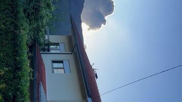 blanco casa con un rojo techo en el montañas en contra el fondo de un enorme nube terminado el montaña el Dom ilumina el nube talón video