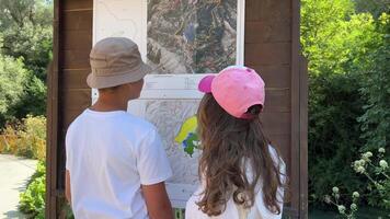 boy and girl looking at a blue eye map of Albania sights on the street in caps on a sunny day teenagers pointing with a finger choosing a place to travel video