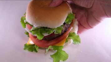 Amazing tasty appetizing burger with various fresh ingredients and buns on a wooden board and paper - unhealthy lifestyle, fast food concept close up 4k footage. Homemade burger and cherry tomatoes. video