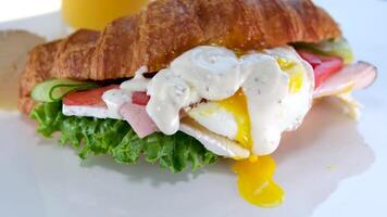 wit saus mayonaise verzuren room heerlijk smakelijk croissant met ei vloeiende dooier vloeiende uit van de belegd broodje vlees tomaat salade en Brie kaas sap Aan een wit bord ontbijt lunch video