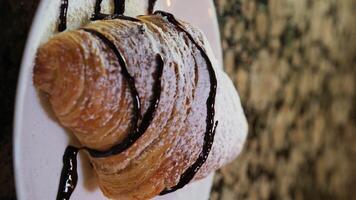 buio cioccolato è versato su un' francese torta, un' dolce e acquolina in bocca dolce su un' di legno asse, un' aromatizzato delizioso con un' cioccolato Riempimento. lento movimento, 4k. verticale. video