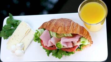 croissant med balyk och gurka sallad löv tomat utsökt frukost med ost och orange juice vit tallrik bacon skikten i smörgås på de balkong på svart tabell utsökt mat lunch mellanmål video