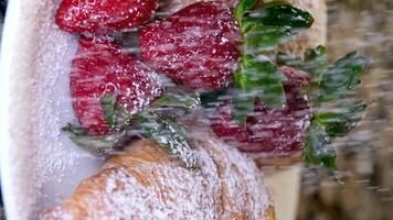 lentamente em pó açúcar granulados dois fresco croissants em uma prato com morangos e hortelã folhas isto neve delicioso irreal lindo verduras branco vermelho francês café da manhã cozinhando restaurante servindo Comida video