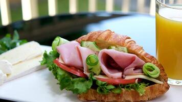 brioche con balyk e cetriolo lattuga le foglie pomodoro delizioso prima colazione con formaggio e arancia succo bianca piatto Bacon strati nel Sandwich su il balcone su nero tavolo delizioso cibo pranzo merenda video