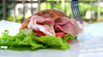 Croissant Sandwich mit Fleisch Jamon Prosciutto mit Tomate Grüner Salat Essen Reich Stücke von Käse im Frühstück Frankreich auf ein Weiß Teller teuer Restaurant Hotel bekommen ein Stück von Fleisch mit ein Gabel video