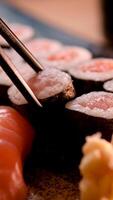 pinnar ta sushi i restaurang lampor bakgrund. mängd av typer sushi med röd kaviar, fisk, philadelphia ost och ätpinnar närbild. uppsättning av utsökt japansk sushi rullar på en sten styrelse video
