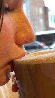 girl face close-up freckles drink hot chocolate cocoa with milk against backdrop of city cars driving winter autumn cold warm up delicious natural product aromatic teenager young real person in cafe video