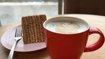 een fietser passeert buiten de venster glas ramen stuk van taart honing taart Aan een roze bord heerlijk lekkernij koffie cappuccino latte in een rood kop Aan een houten tafel traktatie jezelf heerlijk restaurant video